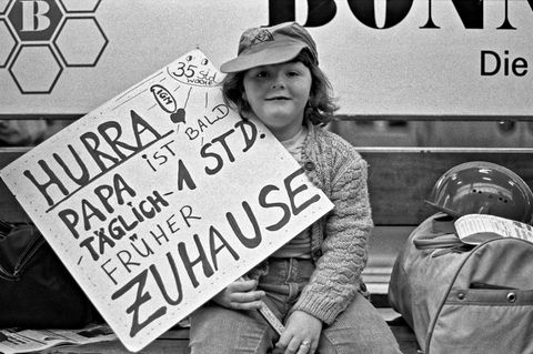 Kind mit Plakat "Hurra, Papa ist bald eine Stunde früher zu Hause"