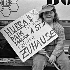 Kind mit Plakat "Hurra, Papa ist bald eine Stunde früher zu Hause"