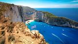 Greek flag on top of majestic cliffs, viewpoint of the famous Shipwreck Navagio Beach, Zakynthos, Greece