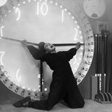 Gustav Fröhlich hängt an den Zeigern einer Uhr