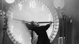 Gustav Fröhlich hängt an den Zeigern einer Uhr