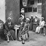 An Tischen im Freien genießen Männer 1922 in der ägyptischen Stadt Esna ihre Wasserpfeifen