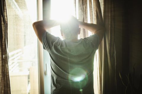 Ein Mann steht am Fenster und schaut hinaus ins Sonnenlicht