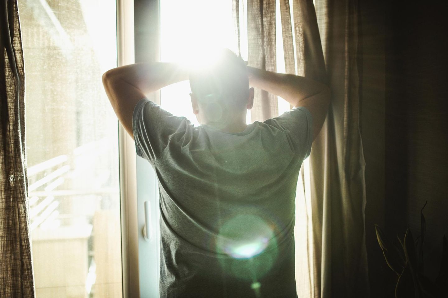Ein Mann steht am Fenster und schaut hinaus ins Sonnenlicht