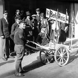 Personen schieben eine Schubkarre, in der jemand sitzt