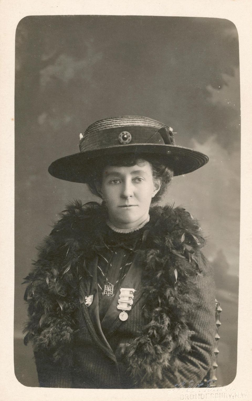 Schwarz-weiße Portraitfotografie einer entschlossen blickenden Frau mit Federboa und großem Hut