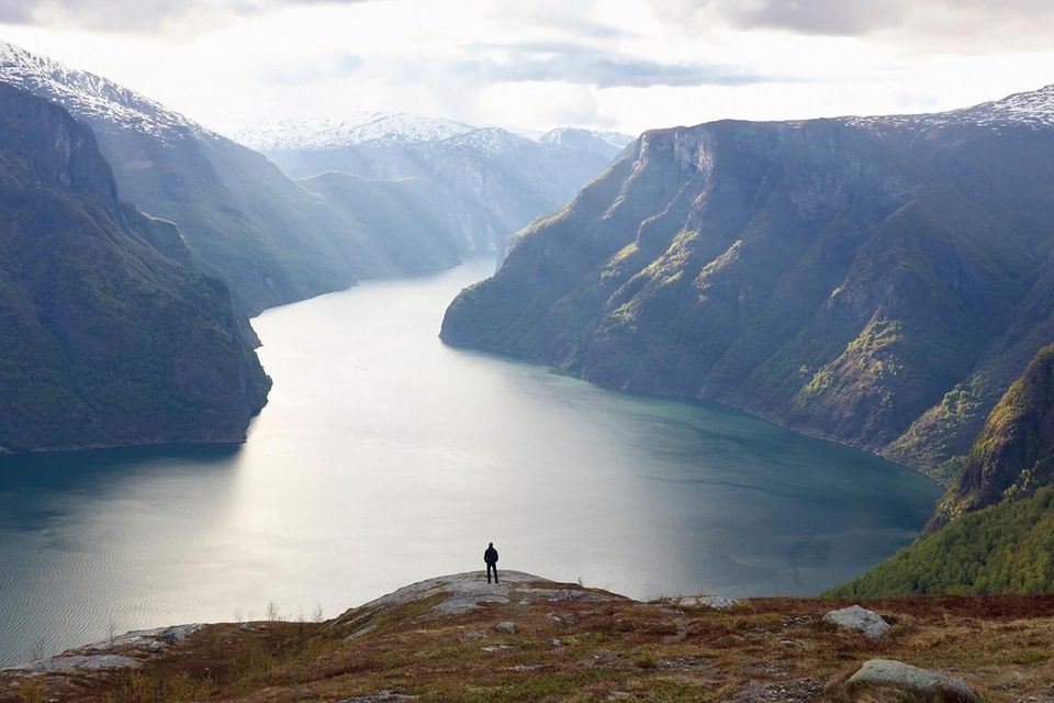 Eine Person steht in einer Landschaft am Fjord 1.2503