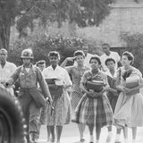 Schwarze Schülerinnen gehen begleitet von einem Soldaten über das Schulgelände auf ein Auto zu