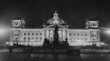 Schwarz-weiß-Aufnahme des erleuchteten Reichstagsgebäudes aus dem Jahr 1928 mit Denkmal davor und Kuppel