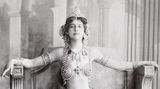 Frau im exotischen Schleiertanzgewand, das viel Haut zeigt, auf einer Art antikem Thron sitzend; SW-Foto, um 1906