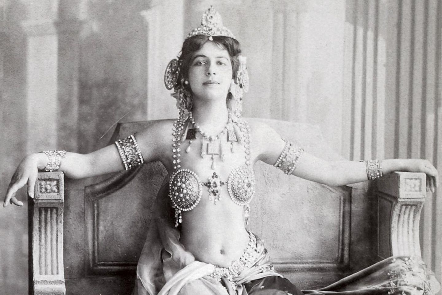 Frau im exotischen Schleiertanzgewand, das viel Haut zeigt, auf einer Art antikem Thron sitzend; SW-Foto, um 1906