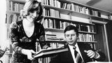 Eine schlanke Frau mit Akten in beiden Händen neben einem kurzhaarigen Mann an einem Schreibtisch, schwarz-weiß, 1970er Jahre