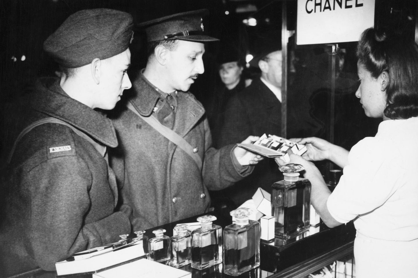 Ein dunkles Kapitel Britische Soldaten an einem Chanel-Stand 1939 in Paris. Nach Ausbruch des Zweiten Weltkriegs schließt Chanel ihre Schneiderei, entlässt alle Näherinnen. Nur ihren besten Geldbringer, das Parfum Chanel No 5, verkauft sie weiter. Unter der deutschen Besatzung Frankreichs kollaboriert sie mit den Nationalsozialisten, beginnt eine Liebschaft mit einem SS-Mann, der als Agent arbeitet, spioniert auch selbst für die Deutschen. Nach der Befreiung Frankreichs wird sie 1944 verhaftet, bleibt aber nur wenige Stunden in Haft. Wie es ihr gelingt, sich so schnell aus den Fängen der Justiz zu winden, ist bis heute unklar.