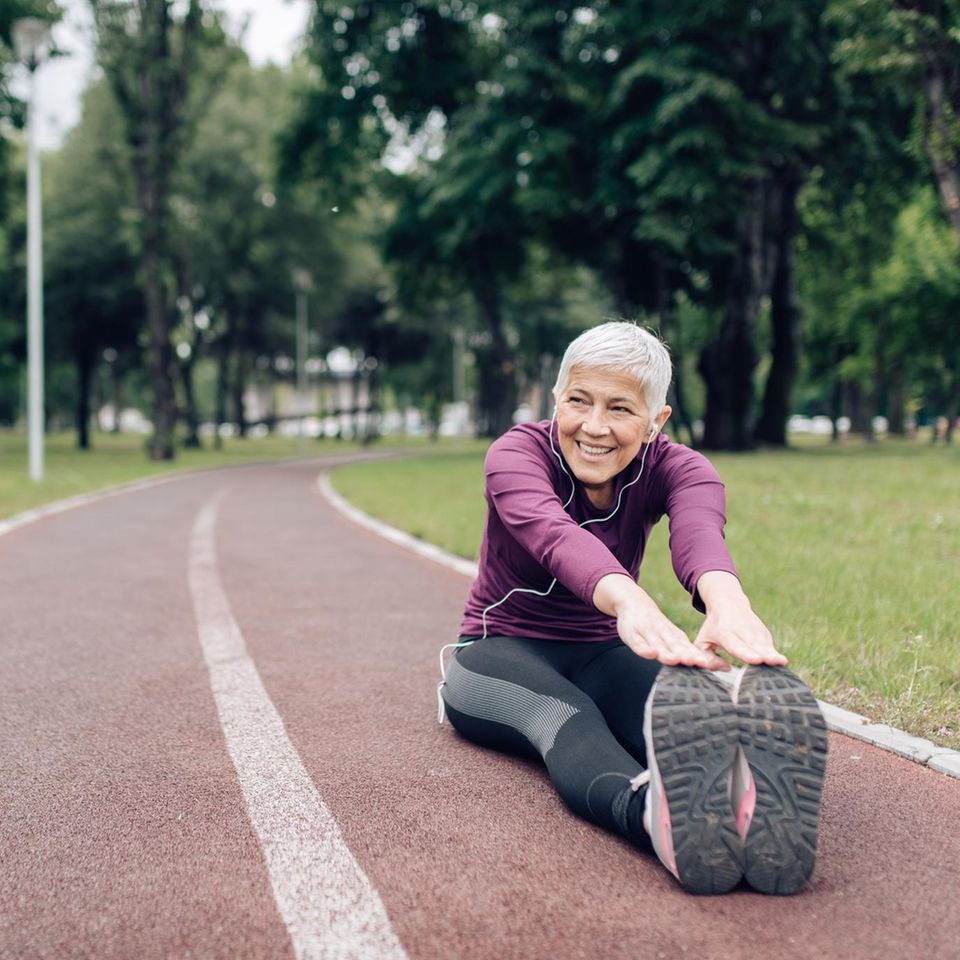 Ältere Frau in Sportkleidung beim Stretching auf einem Sportplatz