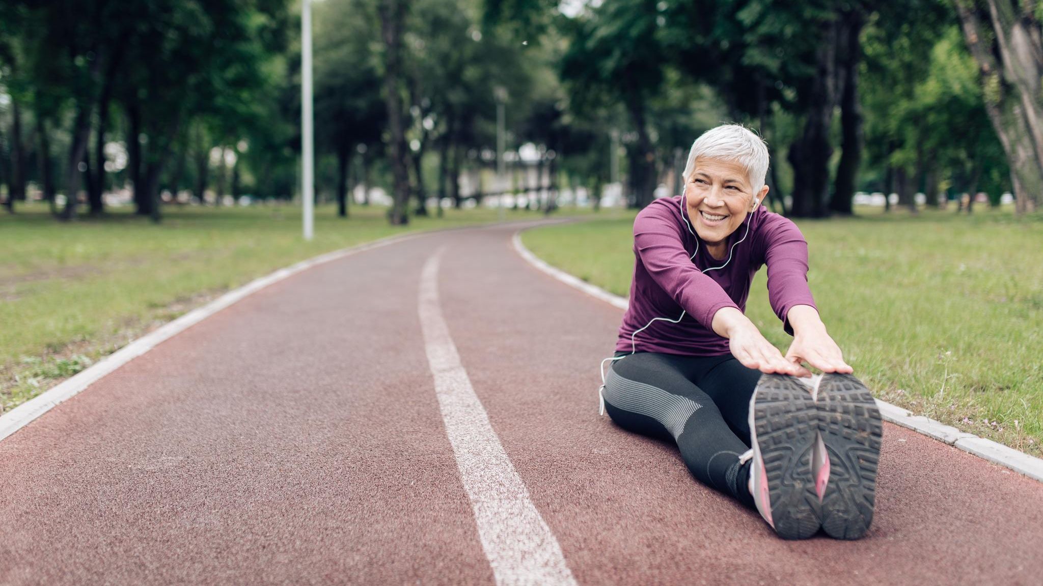 Ältere Frau in Sportkleidung beim Stretching auf einem Sportplatz