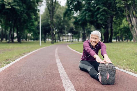 Ältere Frau in Sportkleidung beim Stretching auf einem Sportplatz