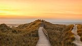 Wooden path and stairs crossing the dunes to the beach of Norddorf on the German North Sea island of Amrum in sunset