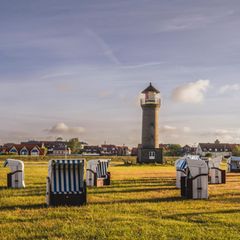 Germany, Lower Saxony, Juist, Hooded beach chairs in front of Memmertfeuer lighthouse