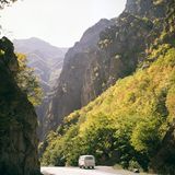 Bulli fährt über Straße zwischen Berghängen