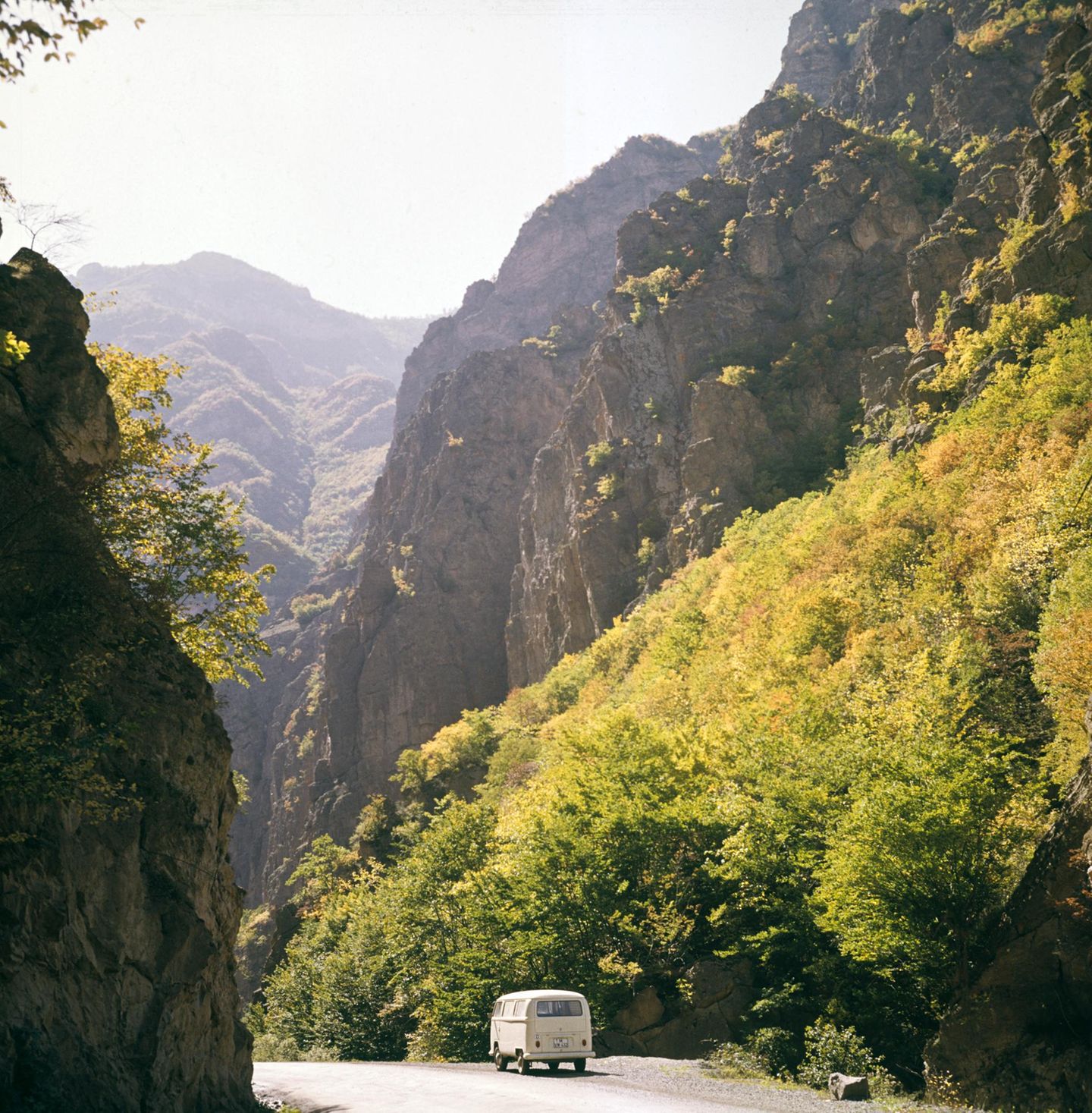 Bulli fährt über Straße zwischen Berghängen