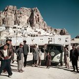 VW Bulli umringt von Menschen vor Hochgebirge