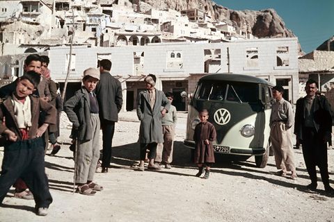 VW Bulli umringt von Menschen vor Hochgebirge
