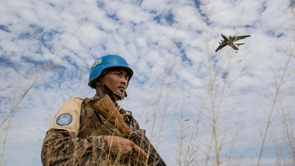 Ein Flugzeug der Vereinten Nationen wirft 2015 Hilfslieferungen über dem Südsudan ab. Ein mongolischer Blauhelmsoldat steht Wache