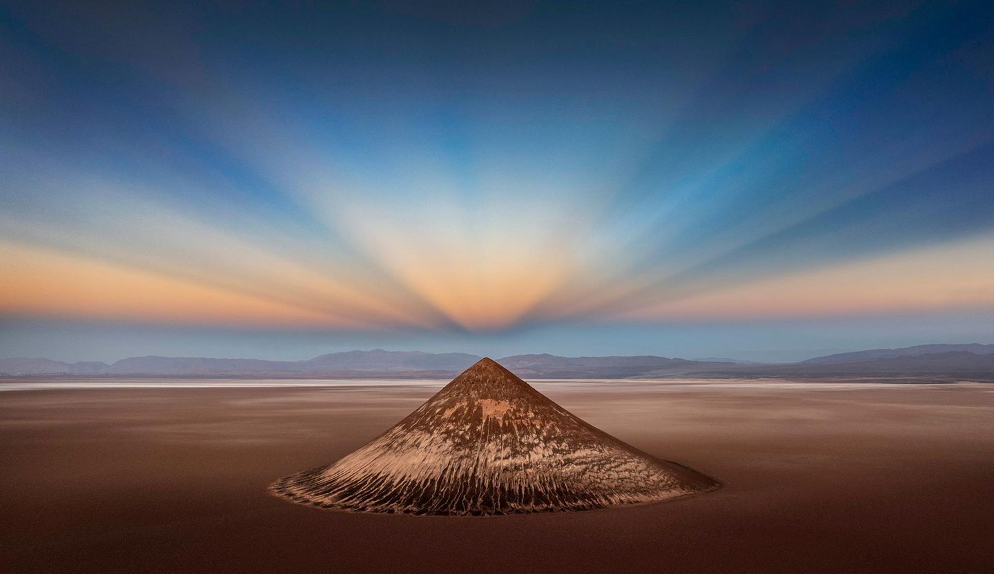 Geometrie des Lichts Surreal: Die Natur formte diesen geometrisch perfekten Bergkegel, der auf 3500 Metern über den Salzfeldern der argentinischen Anden thront. Noch magischer wirkt Cono de Arita im Licht der symmetrisch gespiegelten Gegendämmerungsstrahlen. Sie entstehen, wenn die Sonne kurz vor dem Aufgehen oder direkt nach ihrem Untergang hinter dem Horizont steht. "Es ist ein ganz besonderer Ort mit unglaublichen Möglichkeiten und sehr unterschiedlichen Blickwinkeln", sagt Fotograf Ignacio Palacios. Seine Drohnenaufnahme des Cono de Arita ist das "Foto des Jahres".