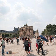 Touristen am Louvre schützen sich mit Schirmen vor der Sonne.