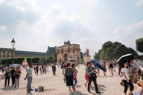 Touristen am Louvre schützen sich mit Schirmen vor der Sonne.