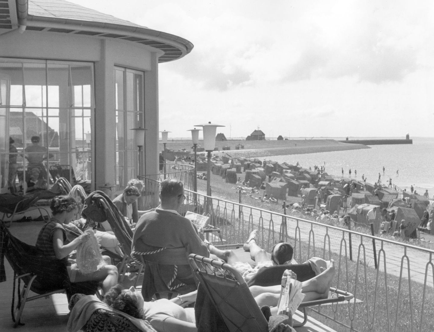 Büsum, 1957 Ein friedlicher Moment am Meer: Die Sonne wärmt die Terrasse der Lesehalle im Seebad Büsum. Aus dem Liegestuhl schweift der Blick über die Reihen von Strandkörben – dahinter liegt die Einfahrt zum Fischereihafen.