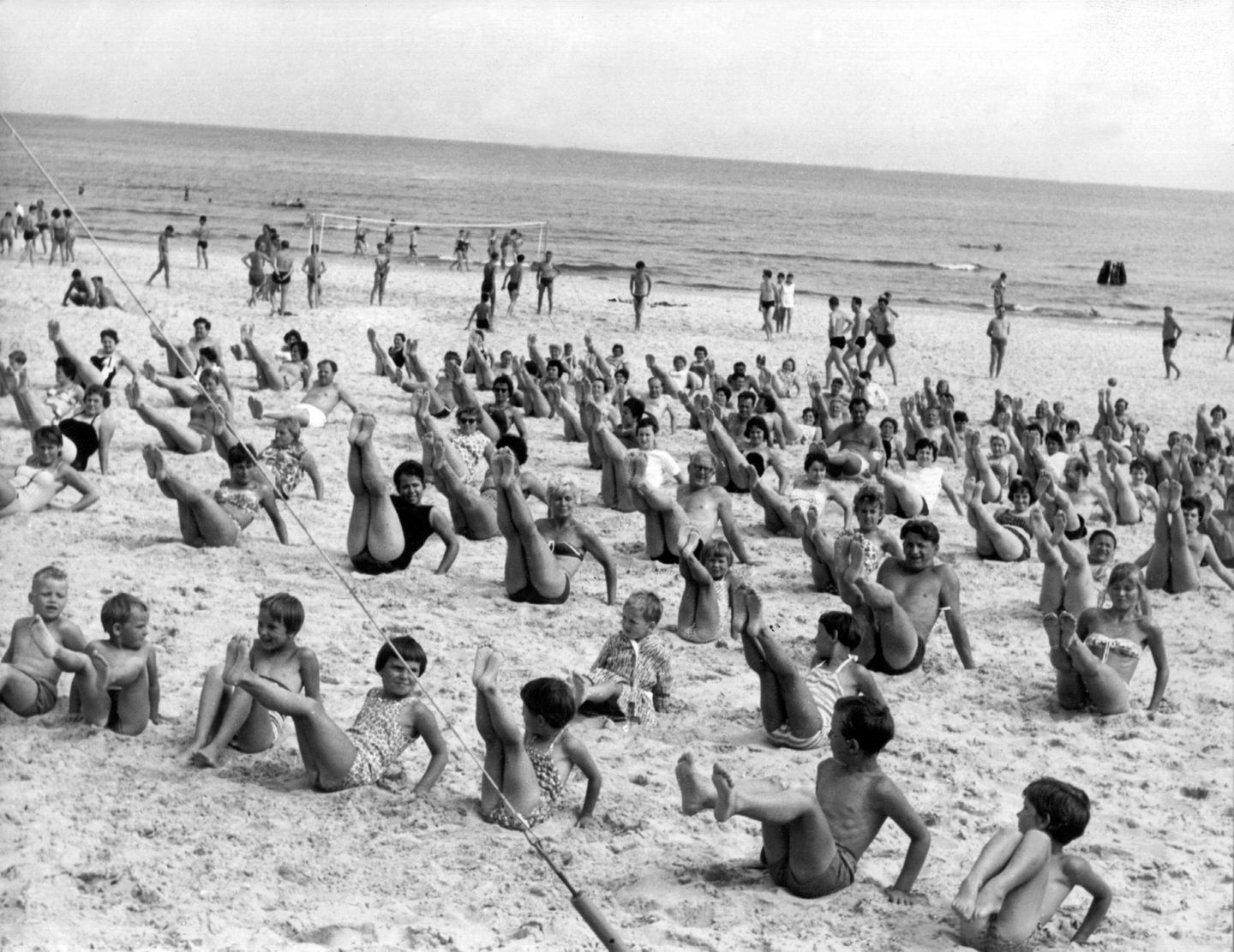 Heringsdorf, 1962 Jetzt nicht nachlassen – der Badekörper soll ja rank und schlank bleiben: Eine Gruppe Urlauber bei der Strandgymnastik unter Anleitung von Sportlehrern im Ostseebad Heringsdorf. Mitmachen kann jede Altersklasse. Seit Saisonbeginn am 15. Mai wird auf drei Plätzen täglich trainiert – bis zum 15. August 1962 nahmen bereits mehr als 10.000 Besucher teil.