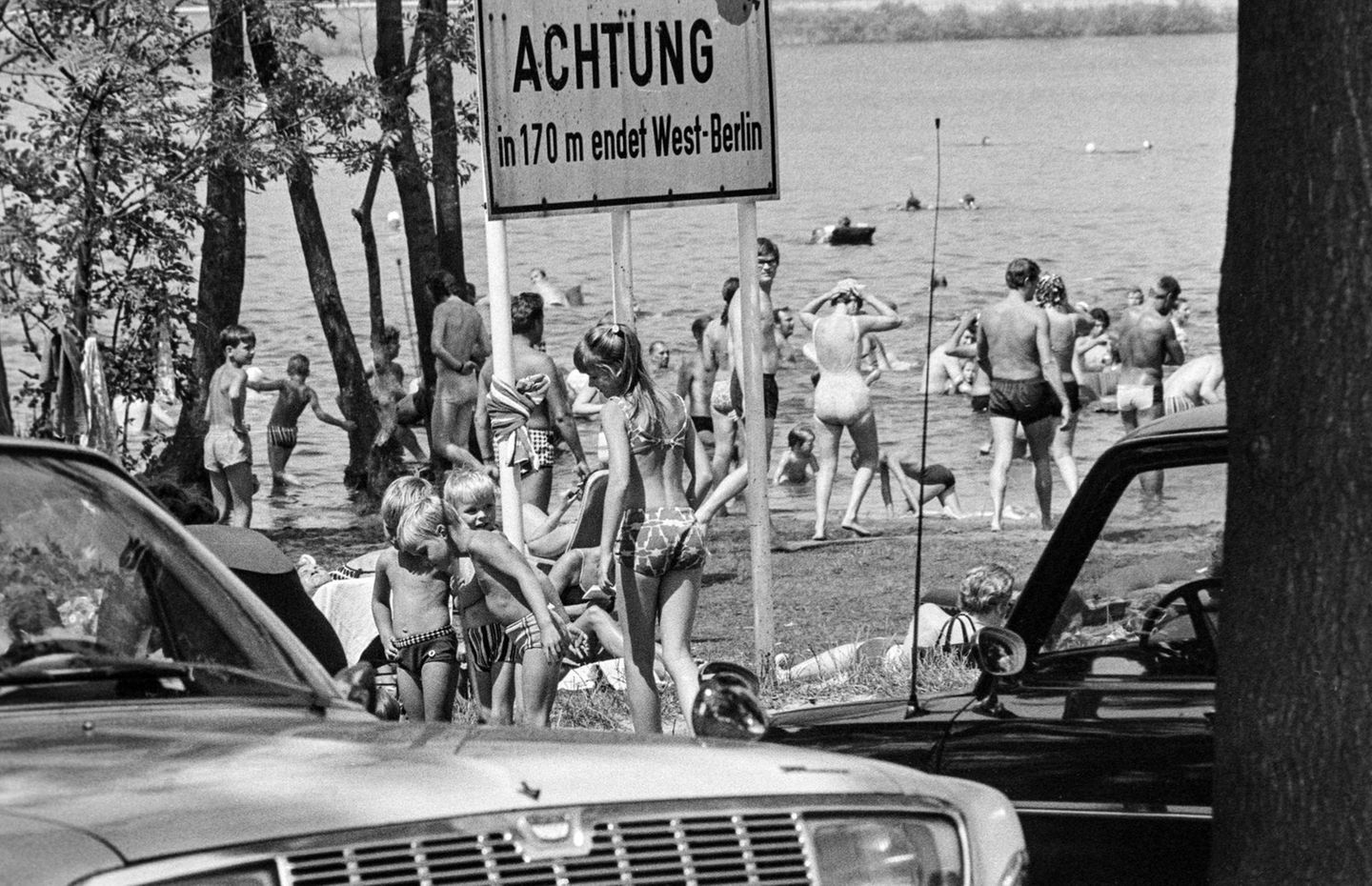 Berlin, 1971 Sommerhitze in einer geteilten Stadt: Westberliner suchen Abkühlung im Glienicker See. Bei mehr als 30 Grad wird das Gewässer im Ortsteil Kladow zur willkommenen Erfrischung. Doch selbst am belebten Badeplatz erinnert ein Schild: Die Grenze ist nah.