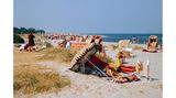 Fehmarn, 1980er-Jahre Die einen stricken, die anderen lesen oder genießen einfach die Sonne: Bei sommerlichen Temperaturen zieht es Badegäste an den weiten Strand der beliebten Ferieninsel Fehmarn.