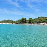 Panoramablick auf Tsoungria, im Vordergrund das Meer, im Hintergrund Strand und Bäume