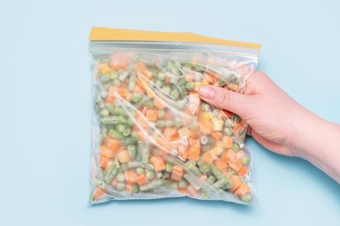 Eine Hand hält einen Beutel mit tiefgekühltem Gemüse