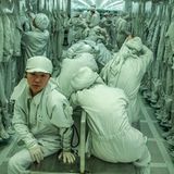 Wanderarbeiterinnen und -arbeiter sitzen in der Umkleidekabine in grünen Anzügen.