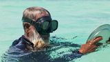 Mann mit Metallteller und einer Taucherbrille im Meer