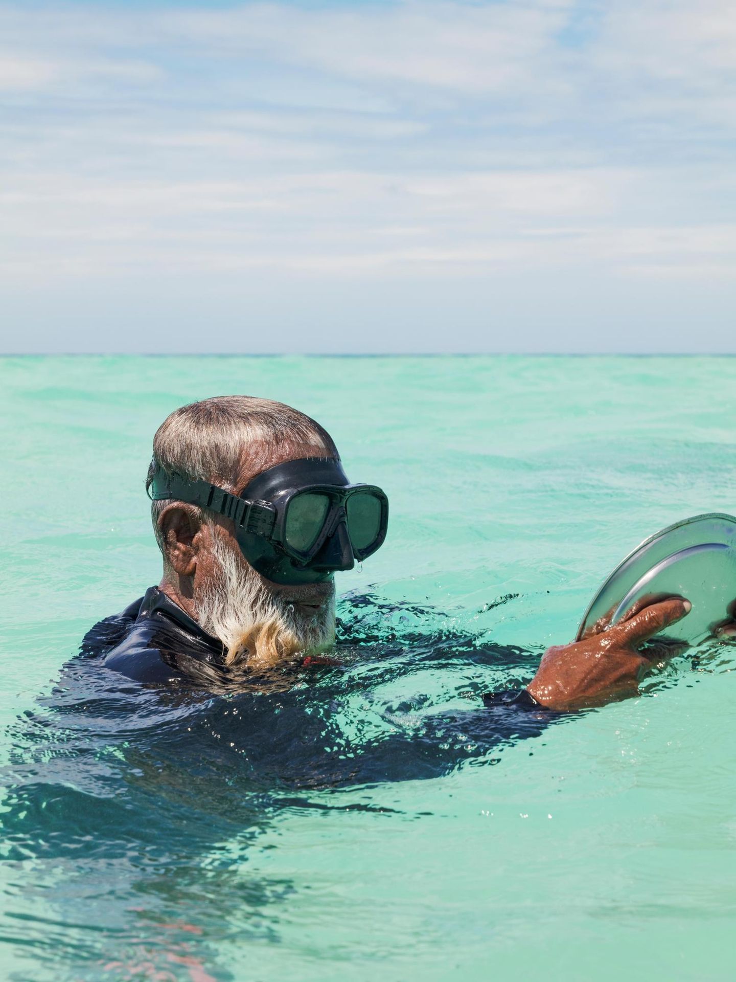 Mann mit Metallteller und einer Taucherbrille im Meer
