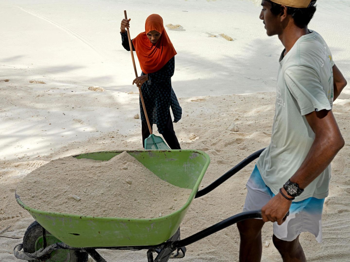 2 Menschen mit Schubkarre im Sand