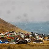 Die Färöer Inseln: ein Ort von wilder Natur und rauem Klima, an dem mehr Schafe weiden als Menschen leben. Durch die nasse Autoscheibe fotografiert, verschwimmen die Häuschen, die sich in einer Talsenke wegducken, zu einer bunten Miniaturlandschaft.