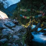 Ein Mann sitzt vor seinem Zelt in den Bergen an einem Fluss