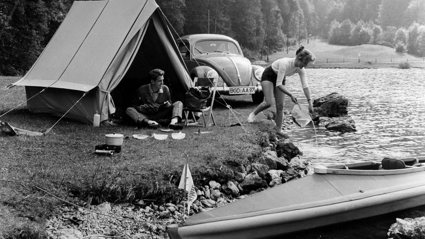 Junges Paar zeltet mit einem Käfer an einem Fluss, 1956