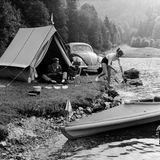 Junges Paar zeltet mit einem Käfer an einem Fluss, 1956