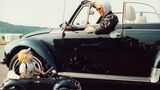 Eine Frau in einem Käfer-Cabrio und ein kleines Kind in einem Käfer-Kinderauto