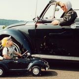 Eine Frau in einem Käfer-Cabrio und ein kleines Kind in einem Käfer-Kinderauto