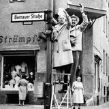 Menschen winken auf einer Leiter an einem Straßenschild 1961
