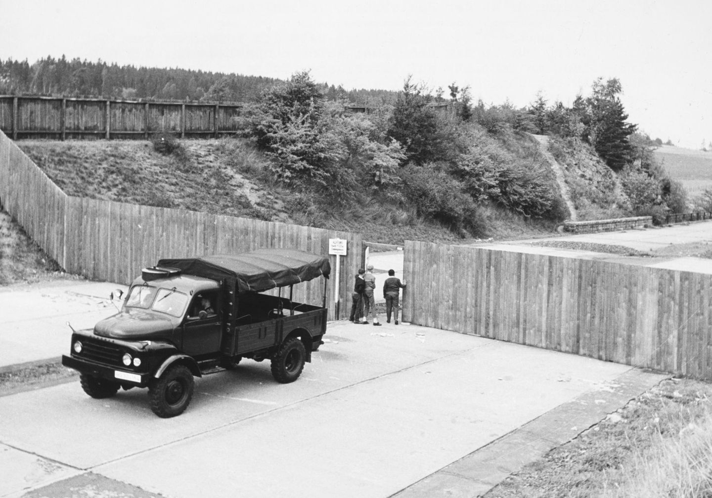 Menschen schauen durch eine Tür in einem Bretterzaun an der Saale-Autobahnbrücke bei Hof, 1962