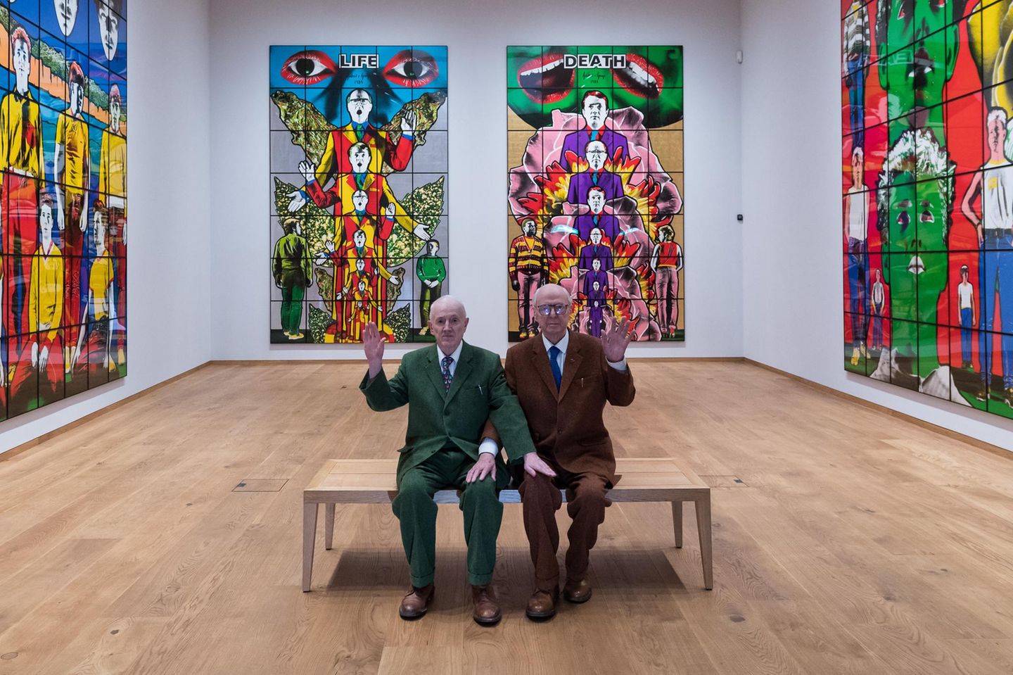 Gilbert & George Gilbert und George sitzen auf einer Bank in ihrer Ausstellung und winken, 2025