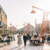 Menschen sitzen vor einem Café, über ihnen schweben rote Lampenschirme